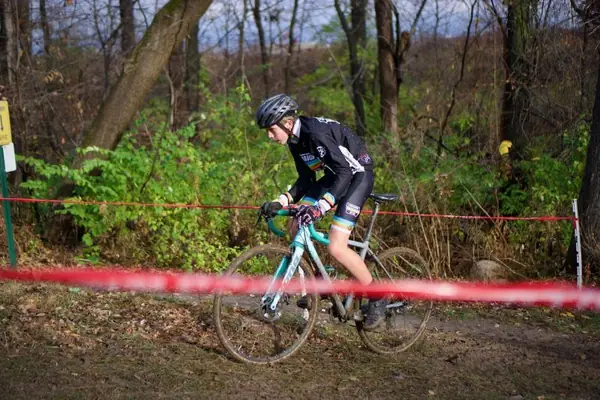 A junior racer riding a dirt section of cyclocross course lined with red tape.
