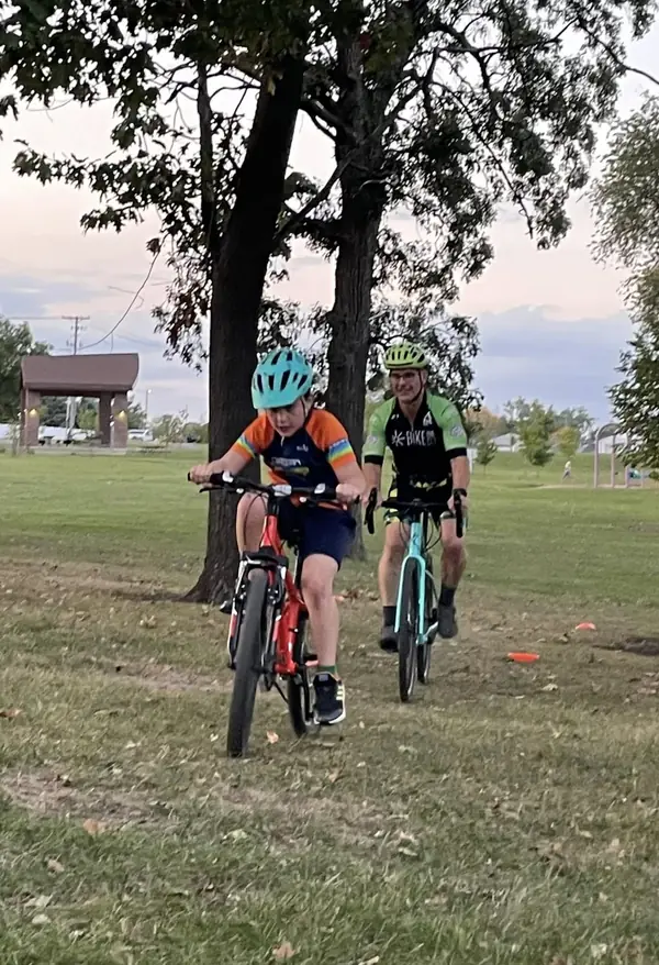A child leads an adult rider along a grass path at dusk, park shelter behind them.